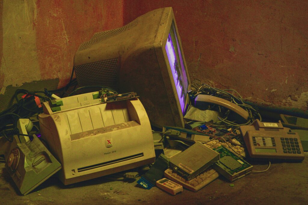 Old electronics pile with a vintage computer and printer in a basement setting.